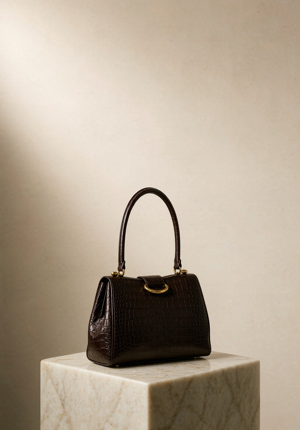 A dark chocolate alligator leather top-handle handbag on a cream marble pedestal